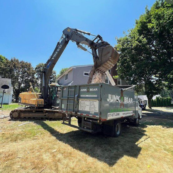 Scoop crane vehicle emptying debris into a Junk Bear dumpster truck