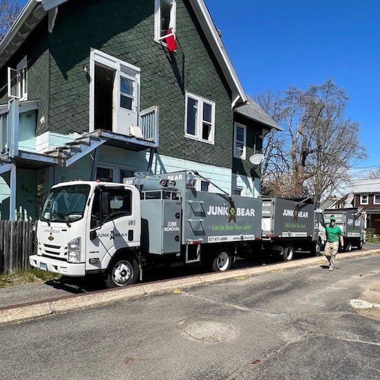 Three junk removal trucks parked outside of a house during a clean out process