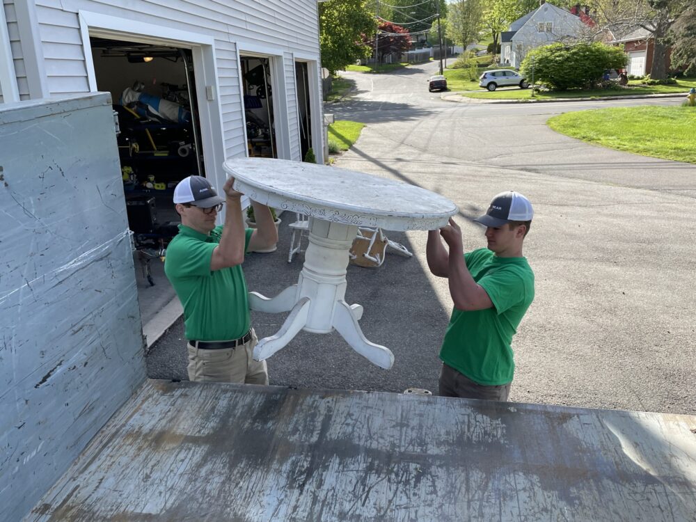 Junk Bear professionals lifting an old table onto the truck during junk removal services in Connecticut